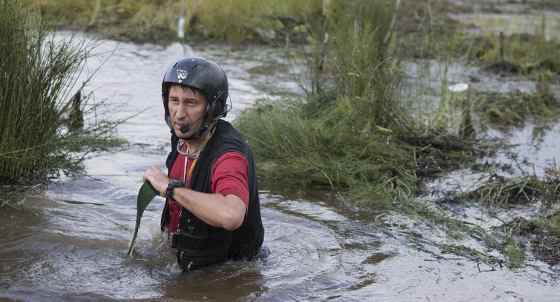 Man wearing helmet and wading across muddy stream